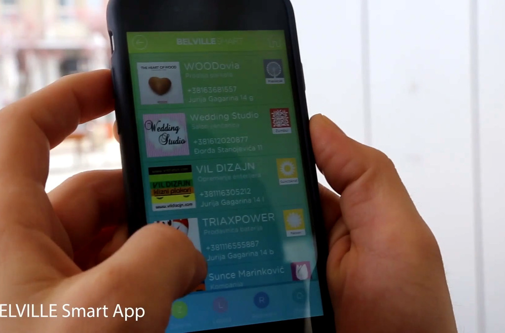 Hand holding a smartphone displaying the Belville Smart App interface with various local business ads, highlighting the app's utility for discovering local services.